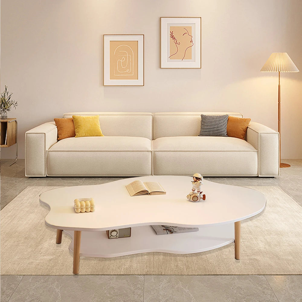 A modern living room scene featuring a cream-colored modular sofa with yellow and gray accent pillows, a white cloud-shaped coffee table in the foreground, and a beige floor lamp on the right against a warm beige wall with two minimalist art prints.