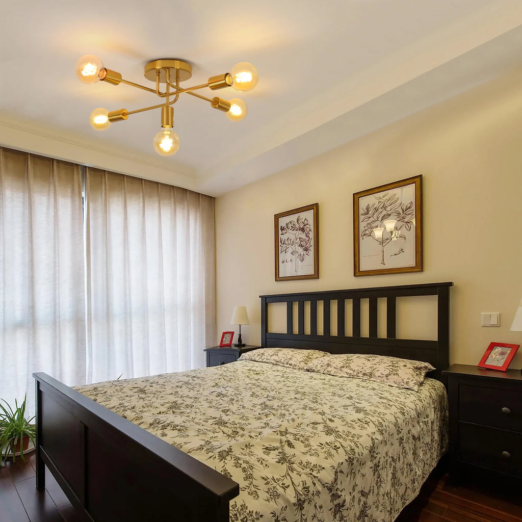 A modern brass multi-arm ceiling light with six glowing bulbs, installed in a bedroom above a dark wood bed with a floral-patterned duvet.