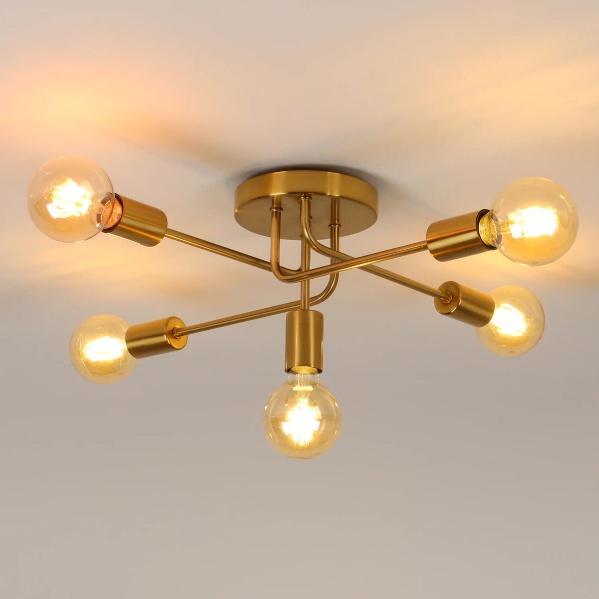 Modern semi-flush ceiling light fixture with a gold brass finish and five exposed filament light bulbs, shown illuminated against a neutral ceiling background.