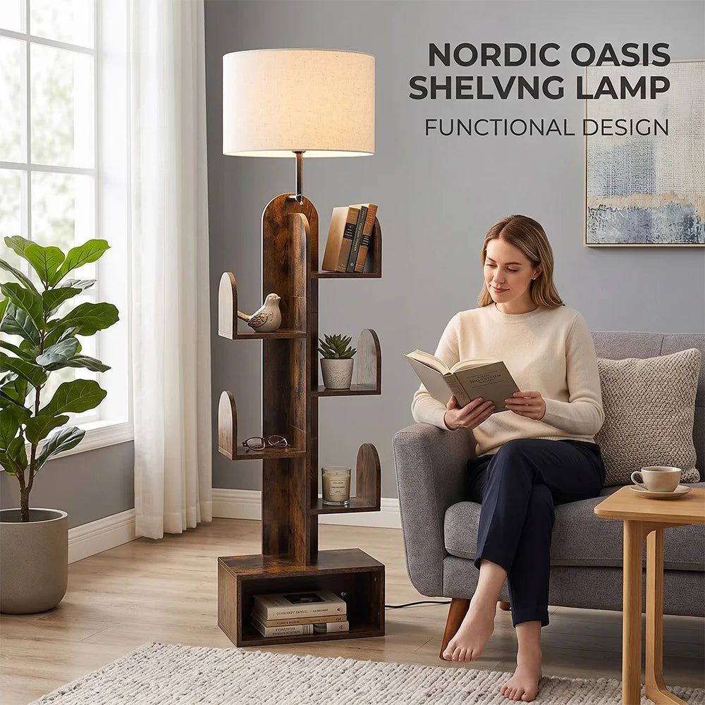 A woman sits on a gray armchair in a living room while reading, with a tall dark wood floor shelf lamp beside her. The lamp has a cylindrical beige shade, curved open shelves with small decorative items, and a cube base.
