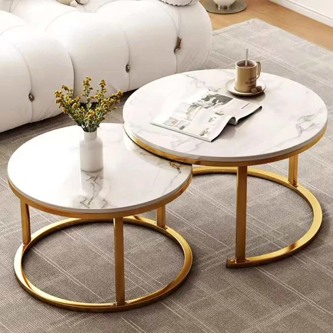 Two round nesting coffee tables with white marble-patterned tops and gold metal frames, styled in a living room setting with a white sofa, gray rug, vase with flowers, and a mug on a saucer.