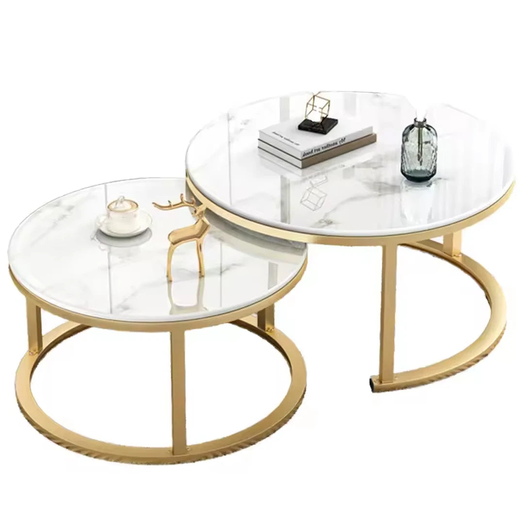 Two round nesting coffee tables with white marble-patterned tops and curved gold metal bases, styled on a clean white background with small decorative objects on top.