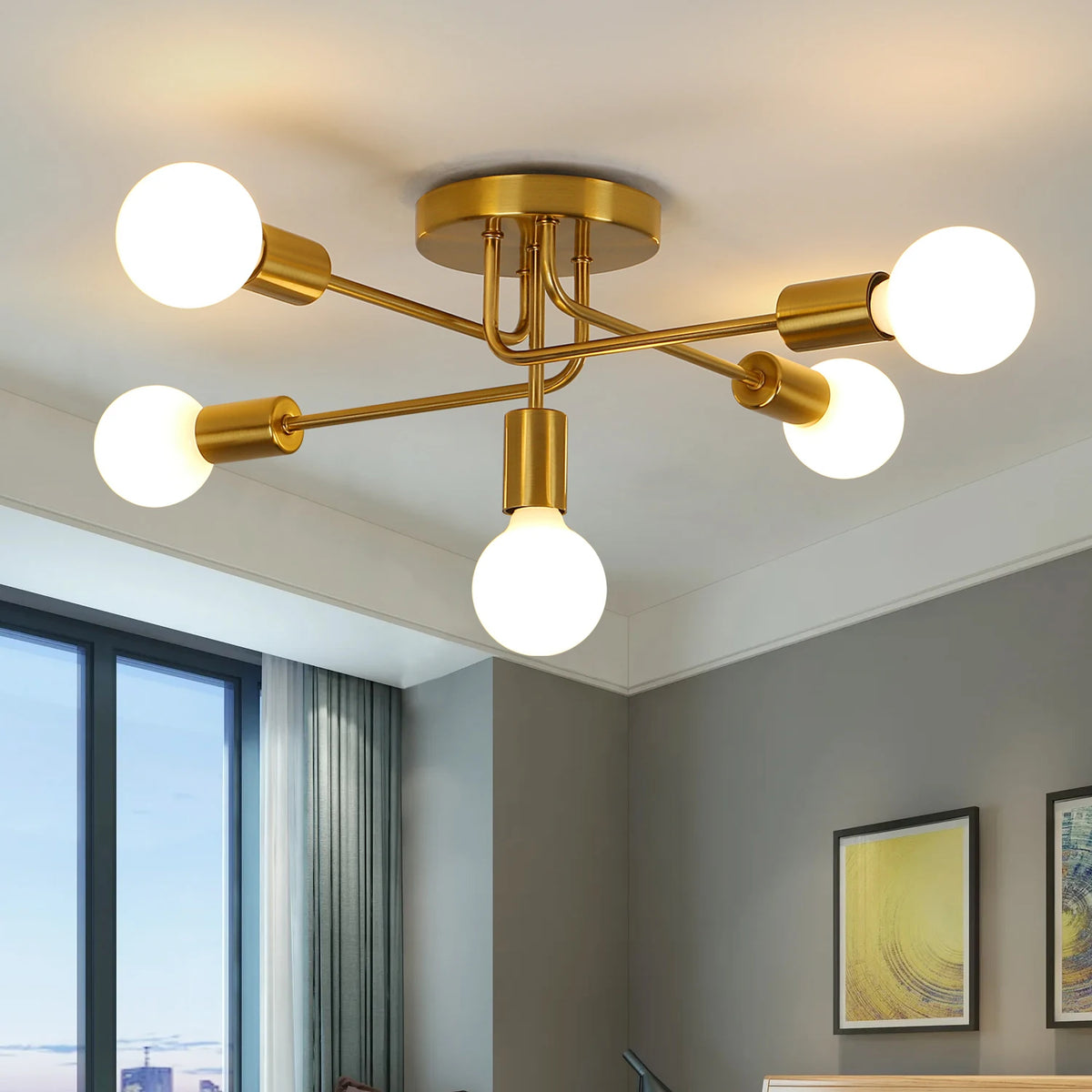 Modern six-light ceiling light fixture with a brushed gold metal frame and spherical glass bulbs, shown installed on a white ceiling in a contemporary room with gray walls and a window.