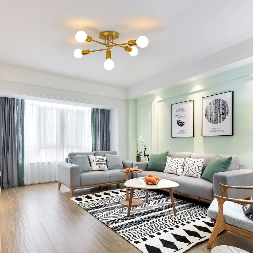 Modern living room featuring a gold multi-arm ceiling light with glowing white globe bulbs, styled with a gray sectional sofa, black-and-white patterned rug, and light green walls.