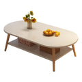 An oval-shaped coffee table with a light beige top and wooden legs, featuring a lower shelf with two woven baskets. Decorative items on the table include a vase with sunflowers and a bowl of oranges, all set against a plain white background.