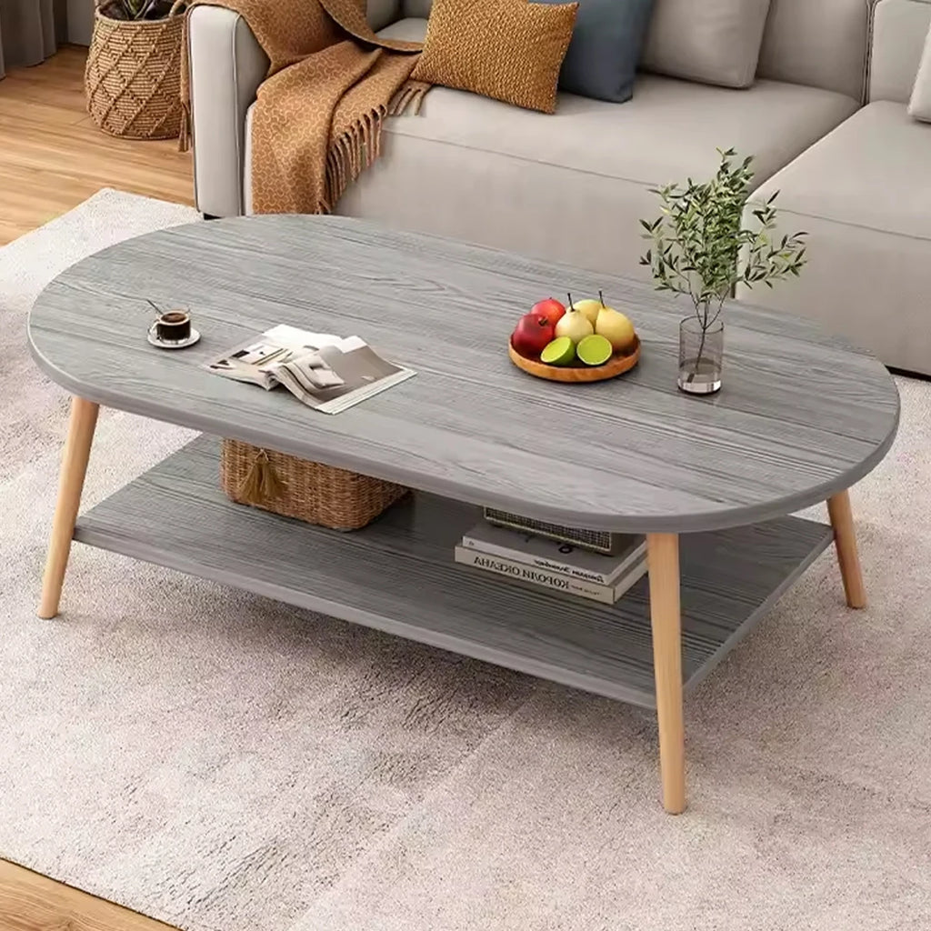 An oval gray coffee table with a wood-grain finish and light natural wood legs, styled in a living room setting with a sofa, throw blanket, and decorative items on top.