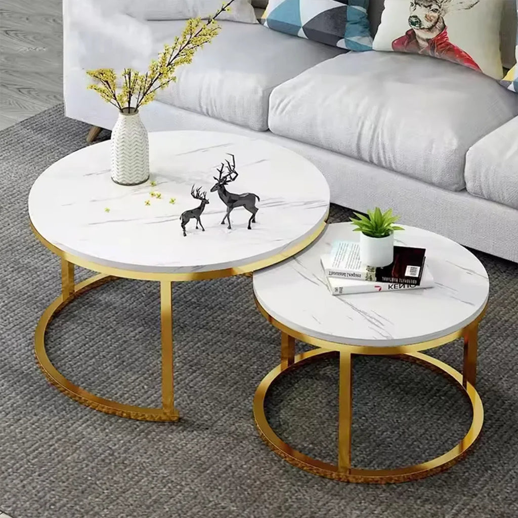 Two round nesting coffee tables with white marble-patterned tops and gold metal bases, styled in a living room setting with a gray sofa and decorative items.