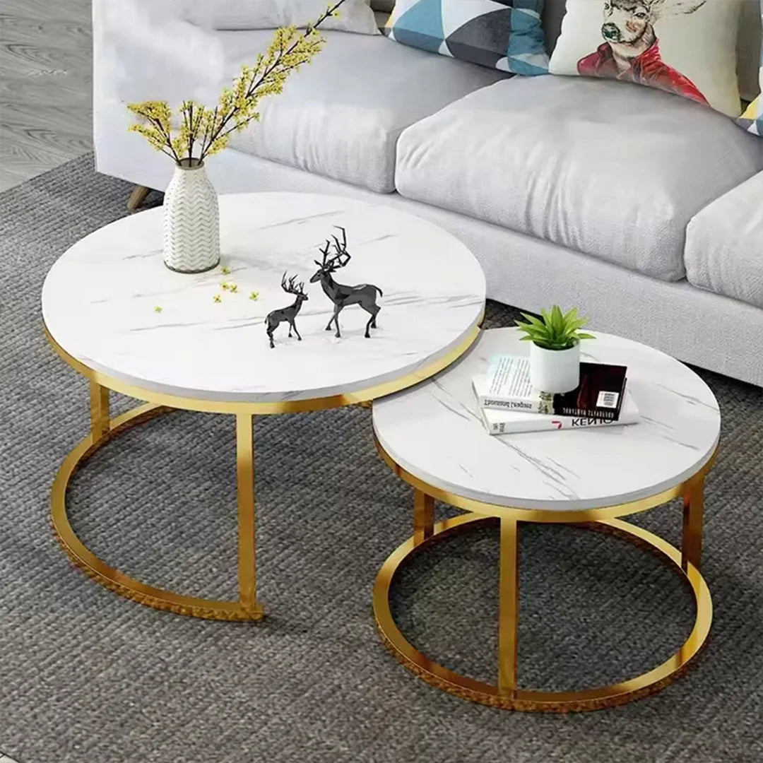 Two round nesting coffee tables with white marble-patterned tops and gold metal bases, styled in a living room setting with a gray sofa and decorative items.