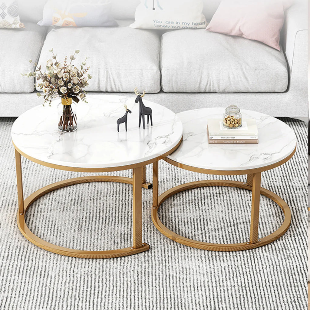 Two round nesting coffee tables with white marble-patterned tops and gold metal bases, styled in a bright living room in front of a light gray sofa.