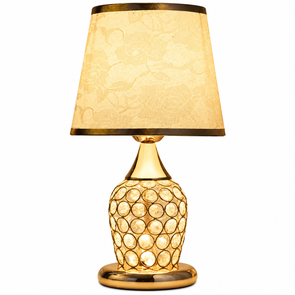 A table lamp with a warm gold-finished base featuring a circular crystal-like pattern, a matching gold-toned neck and base, and a tapered beige fabric shade with a subtle floral pattern and gold trim.