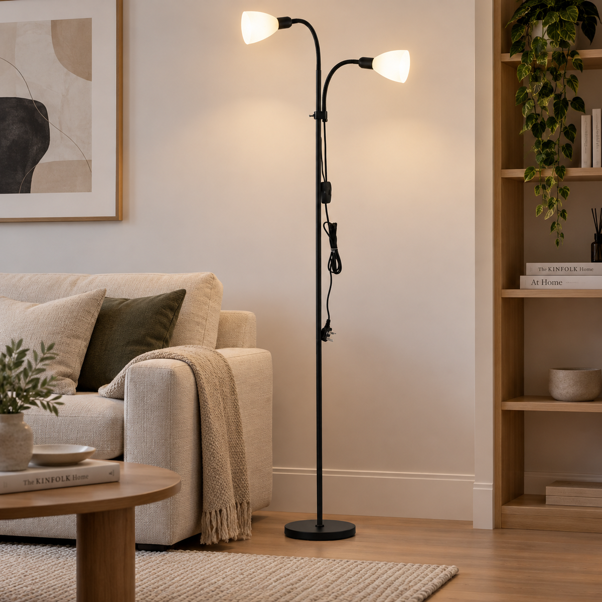 A black adjustable floor lamp with two white globe shades stands in a living room next to a beige sofa and wooden bookshelf.