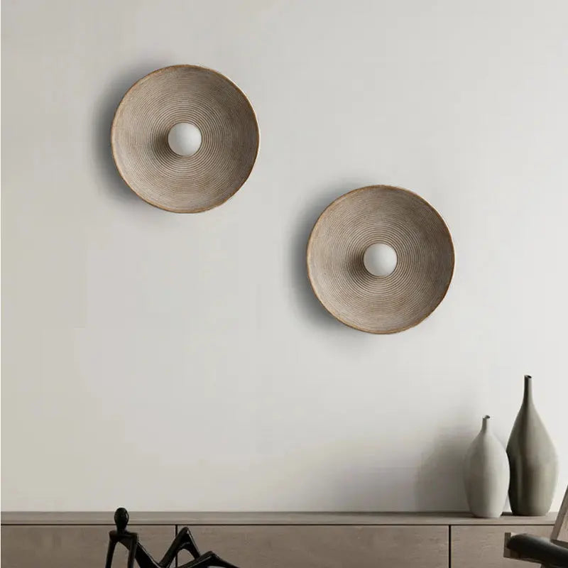 Two round wall decorations on a light gray wall with a shelf below.
