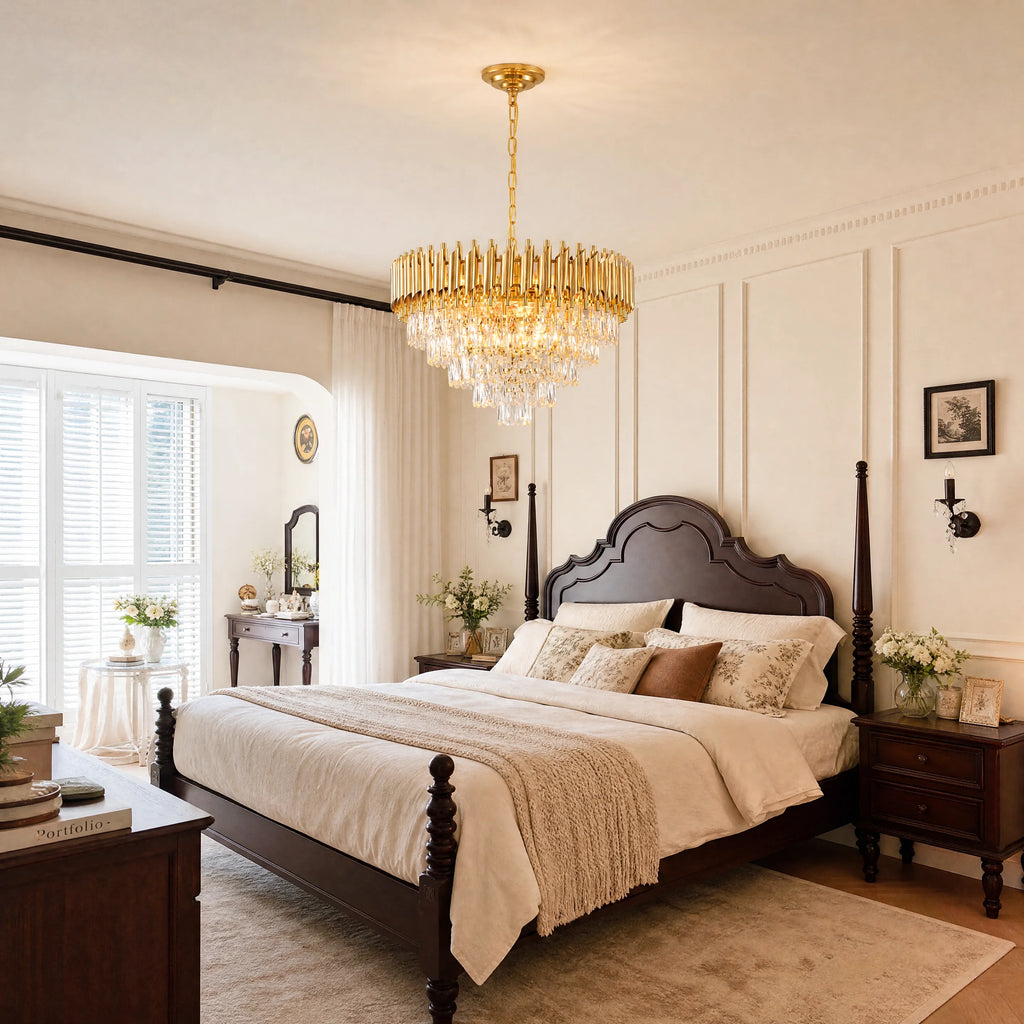A luxury crystal chandelier with a gold-toned frame and clear hanging prisms, suspended from the ceiling in a beautifully decorated bedroom with a dark wood bed and cream walls.