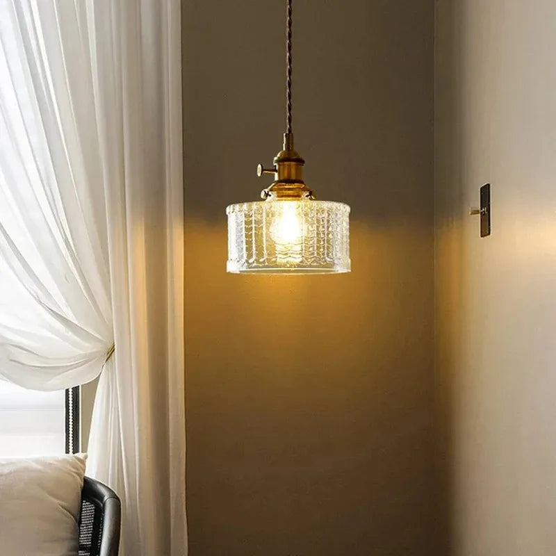 Glass pendant light hanging in a room with white curtains and a neutral wall.