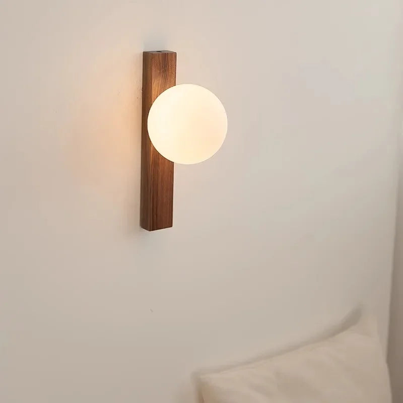 Wall-mounted light fixture with wooden base and round glass shade on a neutral wall.