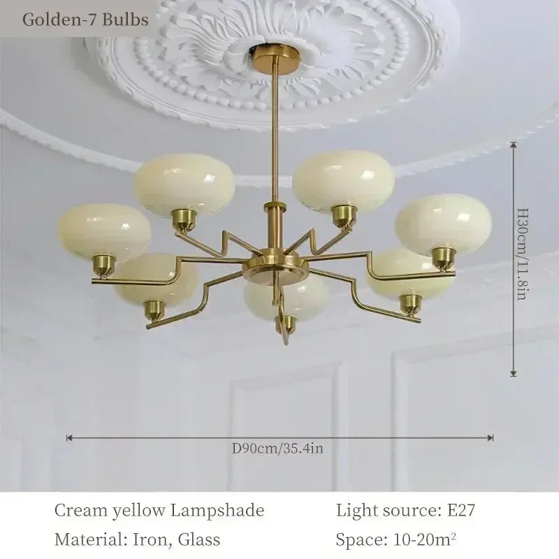 Gold chandelier with cream yellow lampshades on a white ceiling