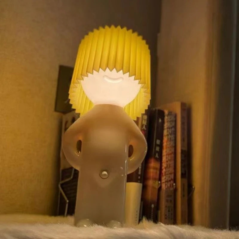 Novelty lamp shaped like a person with a yellow lampshade on a shelf.