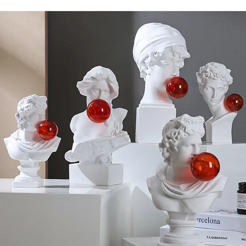 Five white classical bust sculpture lights displayed on white pedestals, each with a glossy red spherical object protruding from its mouth, set against a dark gray and beige background.