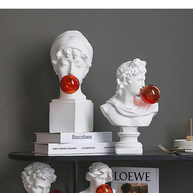 Two white classical-style bust sculptures light with red spherical accents, displayed on a dark shelf against a gray wall.