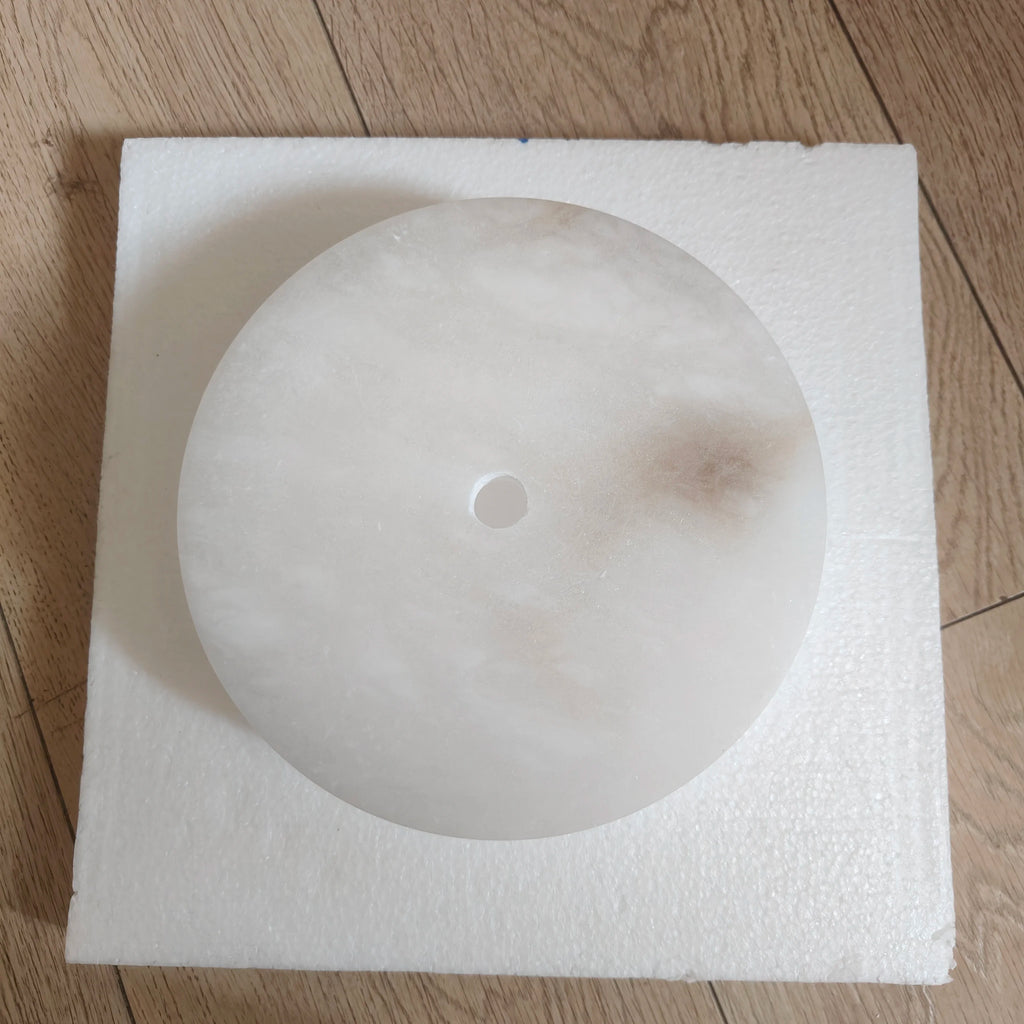 Round ceiling light fixture on a square piece of styrofoam on a wooden floor.