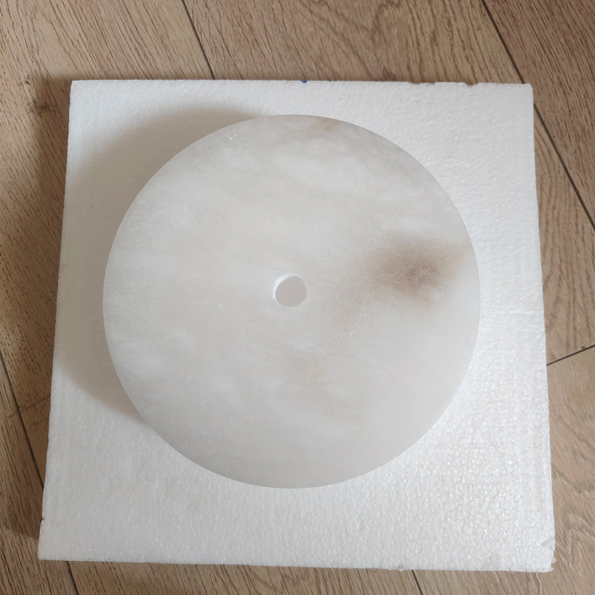 Round ceiling light fixture on a square piece of styrofoam on a wooden floor.