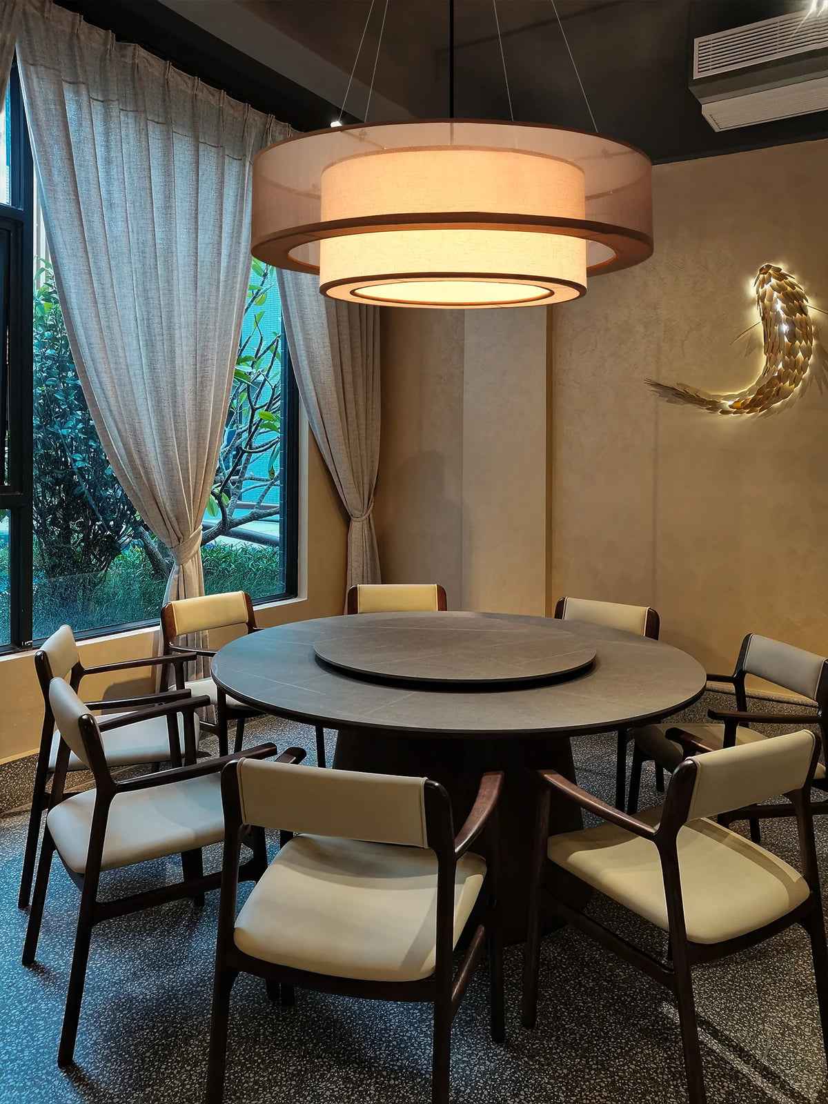 Dining area with round table and chairs in a well-lit room with a drum like ceiling light 