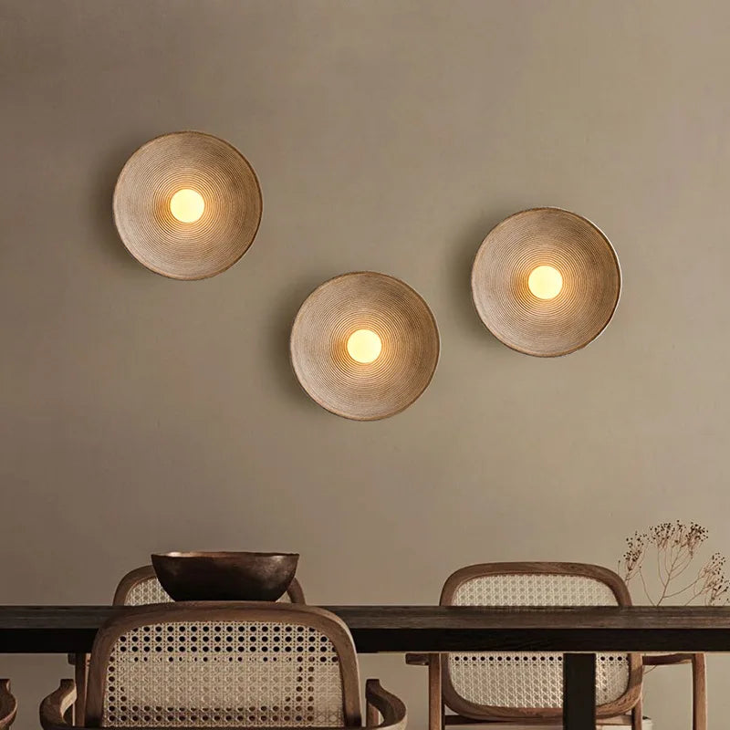 Three round wall lights on a beige wall above a dining table with chairs.