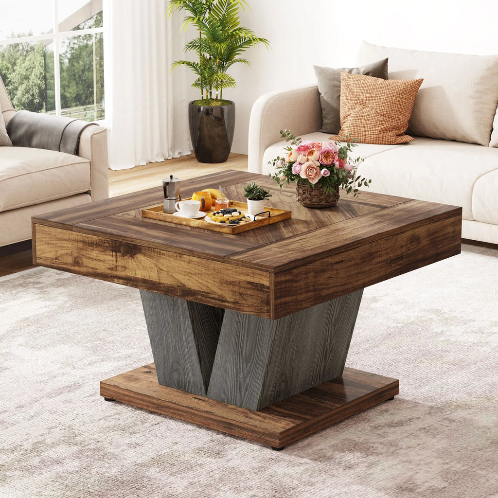 A square wooden coffee table with a dark brown top and base, and a gray V-shaped pedestal center, shown in a bright living room setting with sofas, a plant, and decorative items on top.