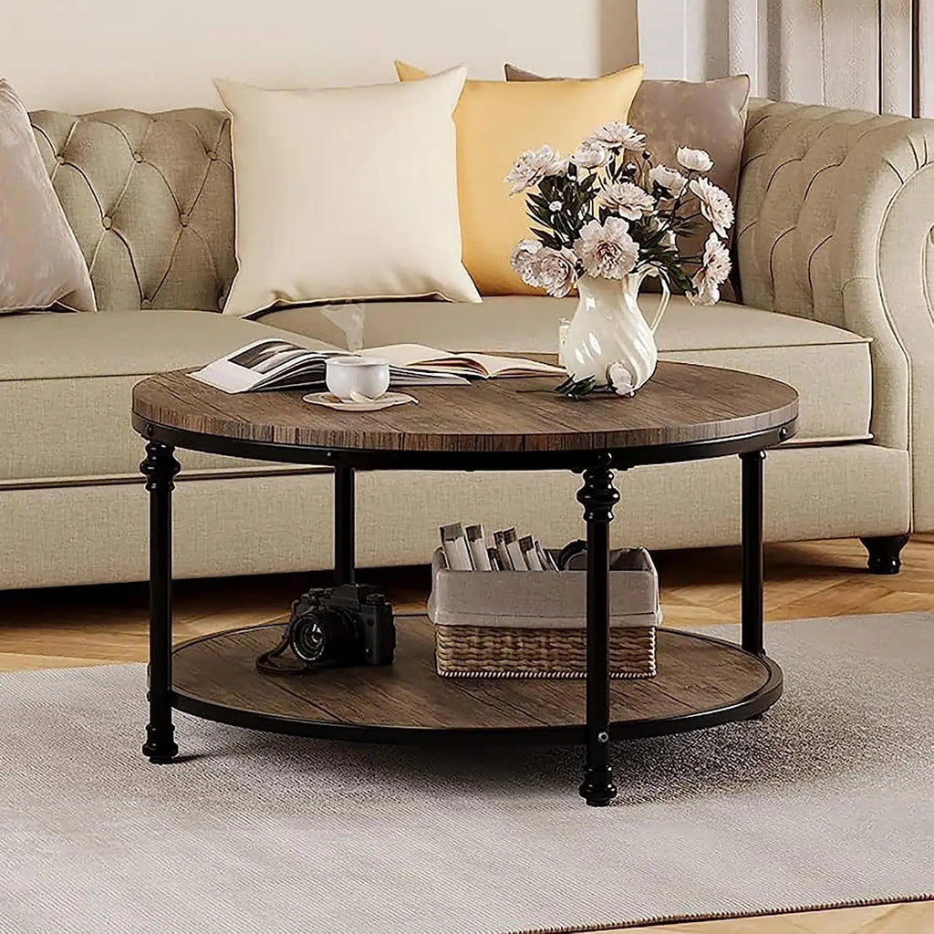 A round two-tier coffee table with a dark wood top and black metal legs, styled in a living room setting with a beige sofa, decorative pillows, a vase of flowers, and other home decor items.