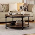 A round two-tier coffee table with a dark wood top and black metal legs, styled in a living room setting with a beige sofa, decorative pillows, a vase of flowers, and other home decor items.