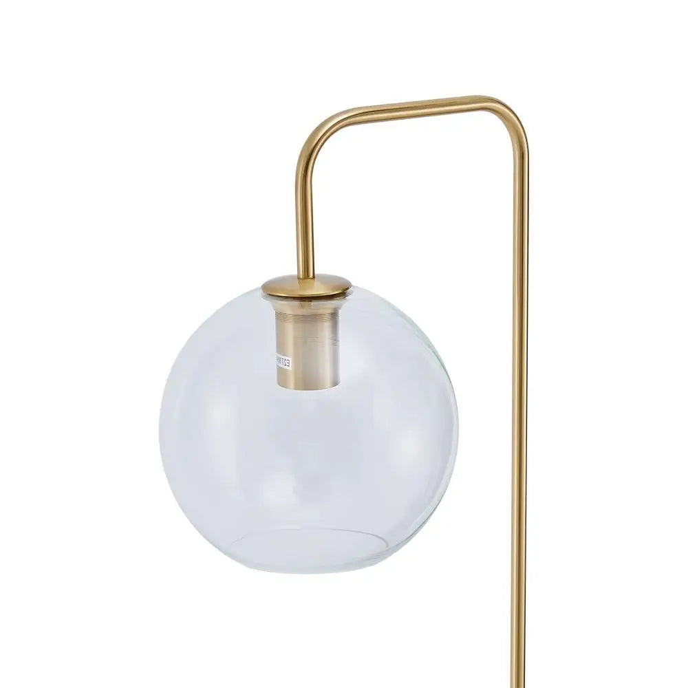 A modern floor lamp featuring a clear glass globe shade and a curved brass-colored metal stand, shown against a plain white background.
