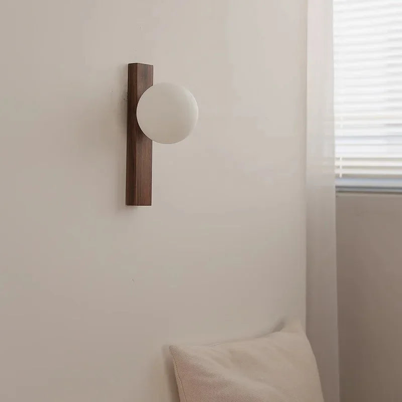 Wall-mounted light fixture with wooden frame and white globe on a neutral wall.