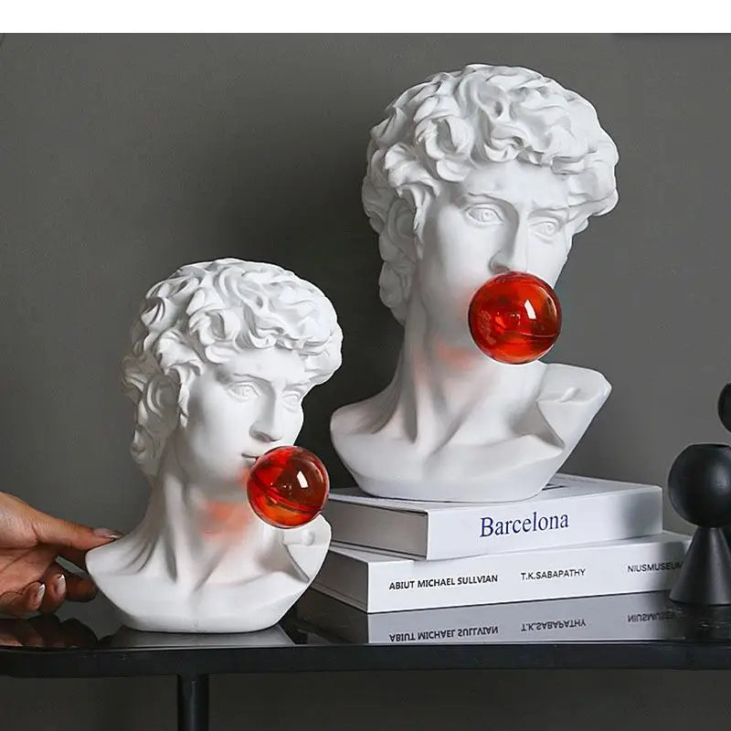 Two white classical bust sculptures resembling Michelangelo's David with red glowing bubbleglobe accents, displayed on stacked books on a dark shelf with a hand entering from the left.