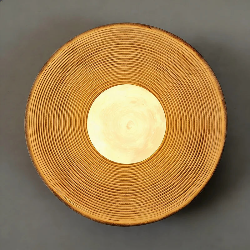 Round woven object with a central light source on a gray background