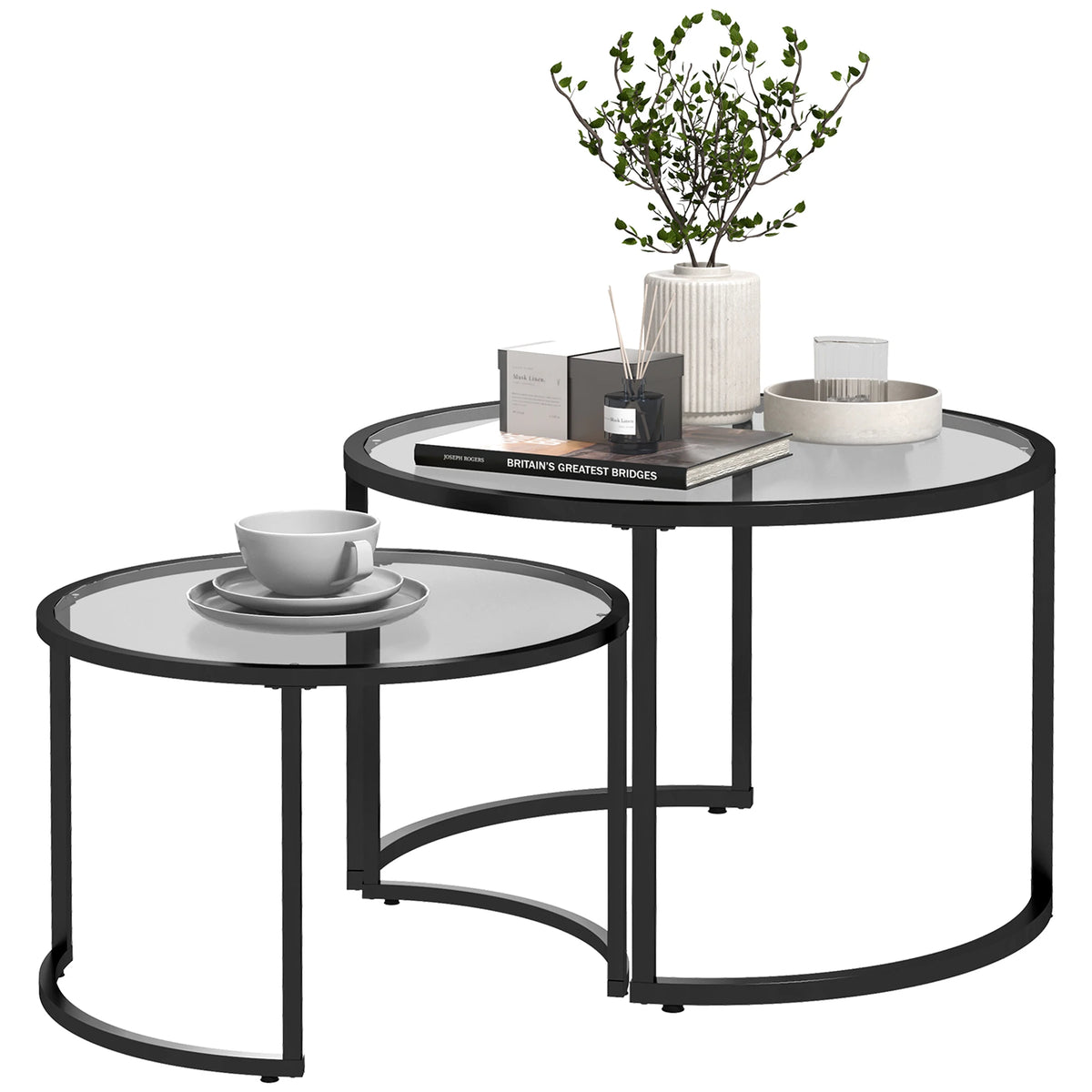Set of two round glass tables with black metal frames, one with decorative items on a white background.