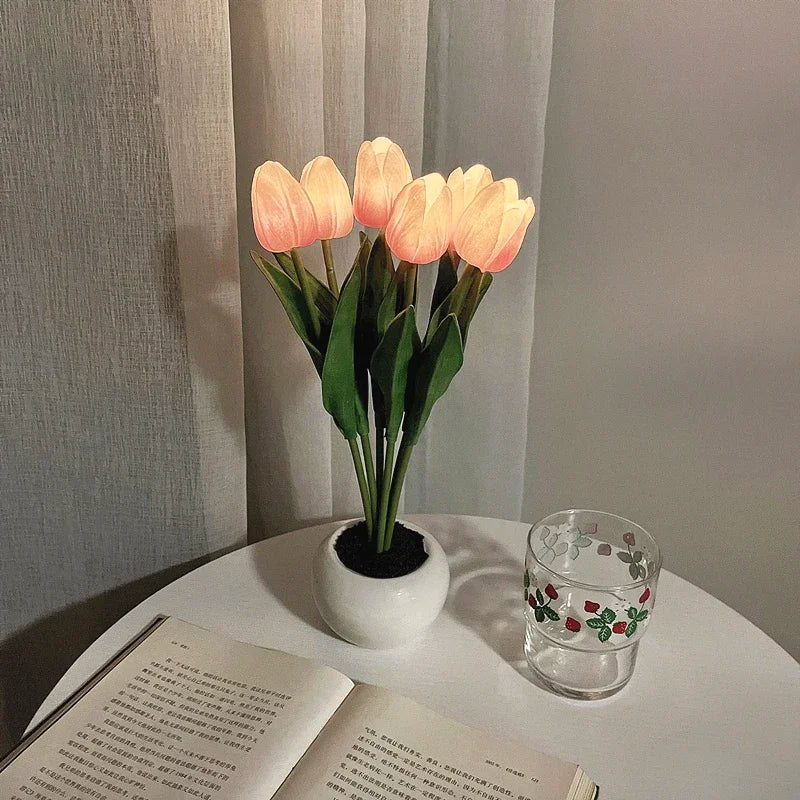 Potted plant like table lamp with glowing pink flowers on a table next to an open book and a glass.