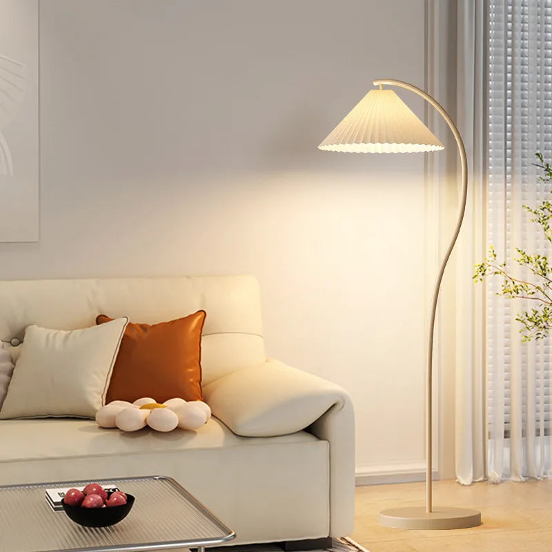 Modern living room with a beige sofa, decorative pillows, a floor lamp, and a small table with fruit.