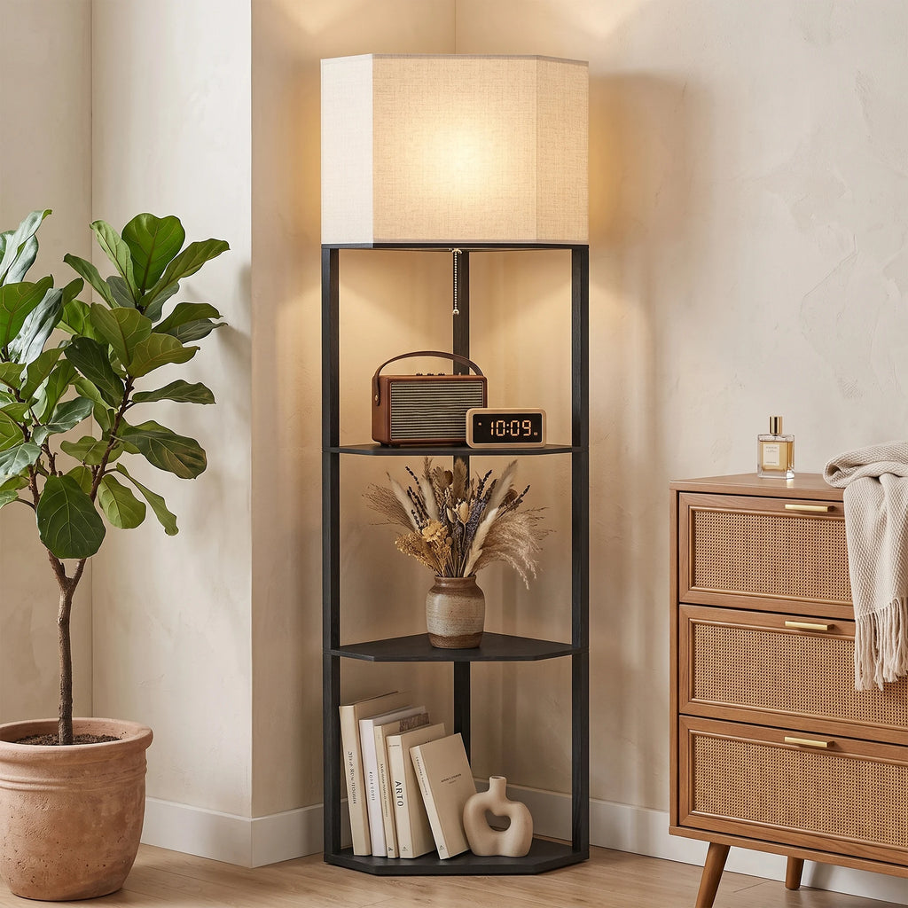 A tall black metal floor shelf with a beige fabric lampshade and three open shelves, styled in a warm beige room next to a potted plant and a wooden cabinet.