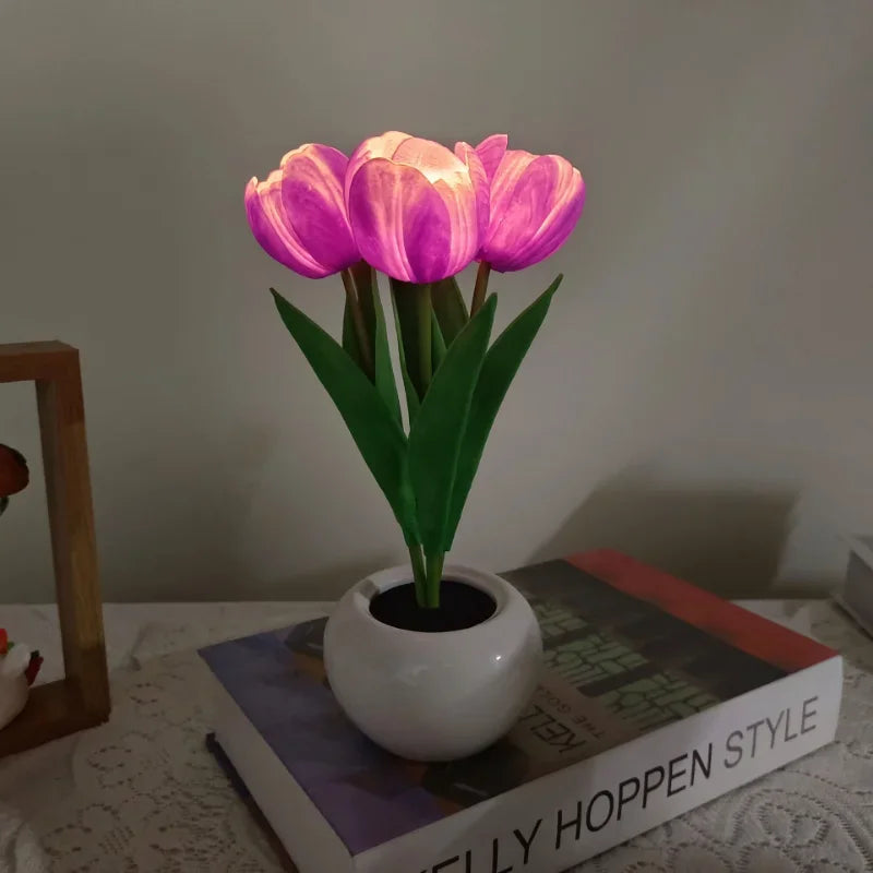 Decorative potted plant like table lamp with pink flowers on a surface with a book titled 'Kelly Hoppen Style'.