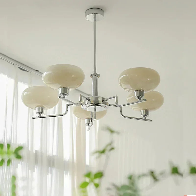 Modern chandelier with beige glass shades in a room with light-colored walls and plants.