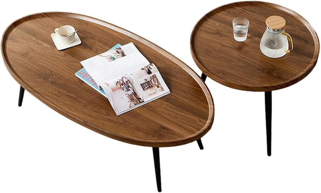 A modern coffee table set featuring an oval wooden coffee table and a round wooden side table with black metal legs, styled with a magazine, a teacup, and a glass carafe on a white background.