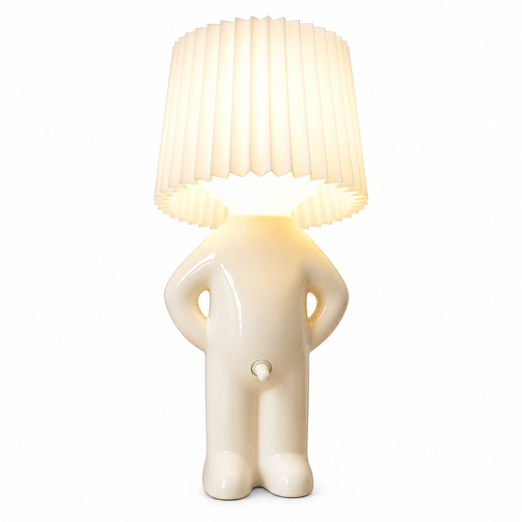 A whimsical table lamp shaped like a small glossy figure with a pleated lampshade for a head, glowing warm white against a plain white background.